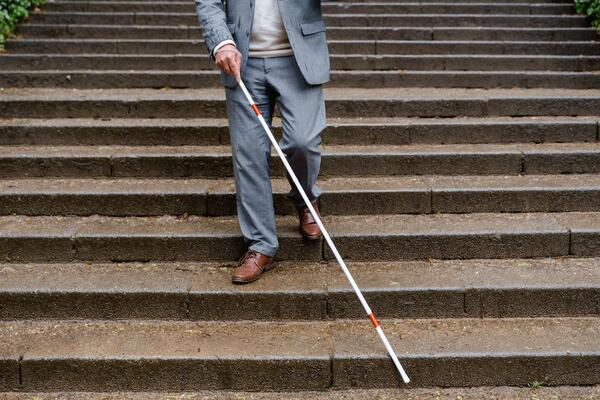 Visually impaired man in suit using white cane navigating outdoor staircase steps illustrating white cane law protections for blind pedestrians in Florida